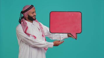 Muslim man shows speech bubble on camera, creating advertisement for new web commercial. Young guy working in marketing industry with isolated cardboard sign, empty billboard. video