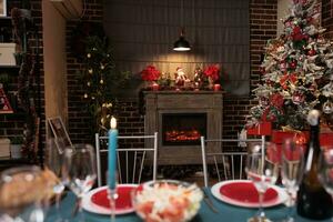 Festive christmas tree near fireplace, home decorated for winter holiday celebration with family at dinner table. Dinning room with fresh food and alcohol glasses for xmas celebration. photo