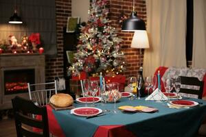 Decorated christmas tree and ornaments near festive dinner table to celebrate seasonal december holiday with family and friends. Dinning party event with traditional meal and wine. photo