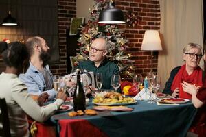 Father and son exchanging presents at christmas dinner, diverse people offering gifts to spread positivity at home. Two men feeling joyful with boxes of goodies on xmas celebration. photo