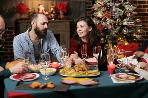 Festive persons celebrating christmas event at table, gthering at home to enjoy traditional food. Diverse friends and family members having fun talking about memories, xmas celebration party. photo