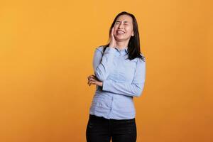 Portrait of cheerful model smiling in front of camera, feeling happy and positive in studio over yellow background. Carefree positive asian woman having positive energy showing playful emotion. photo