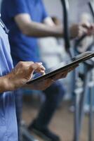 cuidado de la salud especialista en azul matorrales y un estetoscopio es cercanamente examinando un paciente reporte en un tableta en el hospital. médico es participación un digital dispositivo para conductible médico investigación. foto