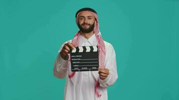 islamisch Erwachsene mit Klappe benutzt zum Aktion nimmt auf Film Herstellung Industrie, jung Kino Produzent mit filmen Produktion Schiefer. Muslim Filmemacher tragen traditionell Kleidung und Schal. video