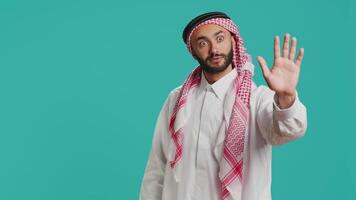 Middle eastern guy doing stop gesture with palm, expressing negativity and refusal in studio. Young male model presenting rejection, being disappointed with stuff over backdrop. video