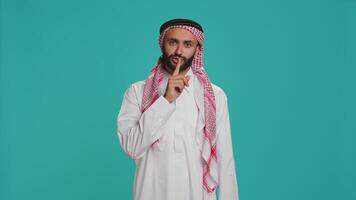Arab man does silence sign with finger over lips, showing hush mute gesture in studio. Private model presenting confidential secrecy symbol on camera, trying to keep secret and privacy. video