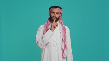 arab man gör tystnad tecken med finger över mun, som visar tysta ner stum gest i studio. privat modell presenter konfidentiell sekretess symbol på kamera, påfrestande till ha kvar hemlighet och Integritet. video