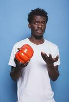 Black man holding red bell pepper in hand to cook meal for healthy diet. African american guy presenting natural vegetable for nutrition and vitamins, standing against isolated background. photo