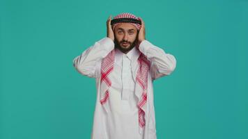 Male model covers eyes, ears and mouth on camera, presenting three wise monkeys symbol. Middle eastern person creating dont hear, see or speak metaphor sign, islamic clothing. video