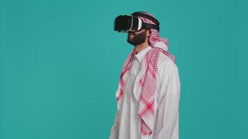 mitten östra kille använder sig av vr glasögon i studio, njuter skjuta med virtuell verklighet simulering på interaktiv headset. ung vuxen har roligt med 3d innovation, modern hobby och enheter. video