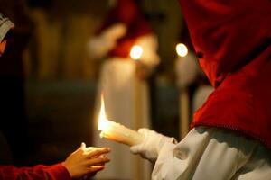 un nazareno en un Pascua de Resurrección noche con un vela y un niño mano foto