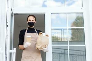 Courier in protective mask and medical gloves delivers takeaway food. Delivery service under quarantine, disease outbreak, coronavirus covid-19 pandemic conditions. photo