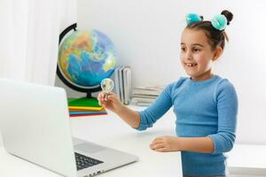 education, school, technology and internet concept - little student girl pointing at laptop pc with light bulbs at school photo