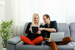 Young couple relaxing on sofa with digital tablet and laptop. photo