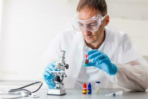 A male doctor or scientist looking through a microscope on a table with laptop computer in background photo