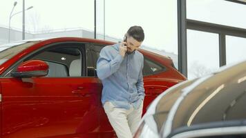 Charming man talking on his smart phone while choosing new car at the dealership video