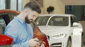 Lycklig man textning på en smart telefon medan handla för ny bil på de återförsäljare video