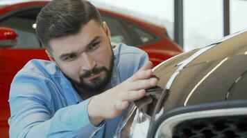 Handsome man smiling to the camera while examining a new car at dealership video