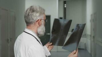 Sénior médecin souriant à le caméra tandis que examiner radiographie scanne video