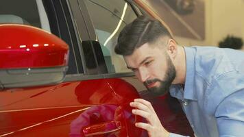 alegre hombre sonriente a el cámara mientras examinando coche a el concesión video