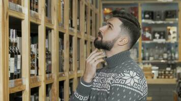 Handsome bearded man looking at the shelves with bottles at wine store video