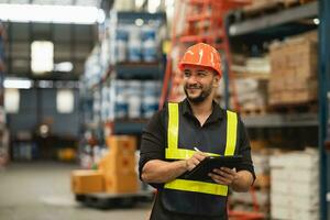 Professional manager man employee smile using tablet check stock working at warehouse. Worker wearing high visibility clothing and a hard hat, helmet and checking and count up goods boxes delivery. photo