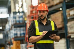 Professional manager man employee using tablet check stock working at warehouse. Worker wearing high visibility clothing and a hard hat, helmet and checking and count up goods or boxes for delivery. photo