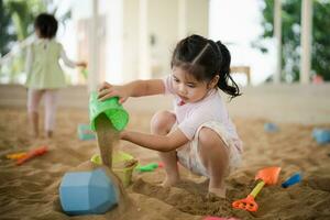 Asian girl children playing sand on the playground in the cafe for kids. Little girl playing in the sand on the playground. Healthy active baby outdoors plays games concept. photo