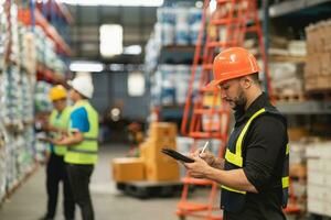 Professional manager man employee using tablet check stock working at warehouse. Worker wearing high visibility clothing and a hard hat, helmet and checking and count up goods or boxes for delivery. photo