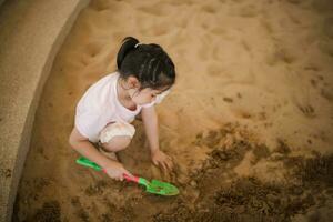 asiático niña niños jugando arena en el patio de recreo en el café para niños. pequeño niña jugando en el arena en el patio de juegos. sano activo bebé al aire libre obras de teatro juegos concepto. foto