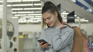 encantador joven mujer utilizando su inteligente teléfono mientras compras a el centro comercial video