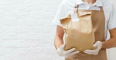 Holding take-out food paper bag, coffee cup. Light grey background, place to insert your text. Delivery man. photo