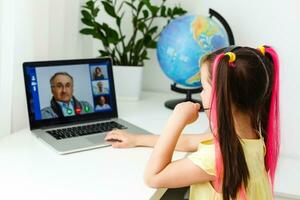 Cool online school. Kid studying online at home using a laptop. Cheerful young little girl using laptop computer studying through online e-learning system. Distance or remote learning photo