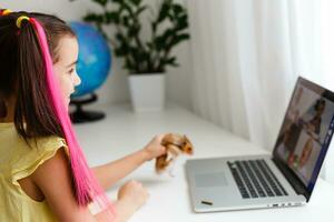 Cheerful young little girl with a pet hamster using laptop computer studying through online e-learning system at home. Distance or remote learning photo