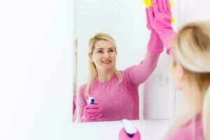 sonriente mujer limpieza un espejo en un baño a hogar foto