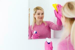 Smiling woman cleaning a mirror in a bathroom at home photo