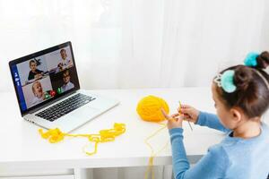 niña tejido de punto a hogar en un ordenador portátil en línea, distancia aprendizaje foto