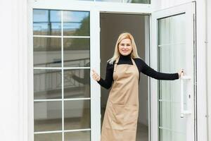 Half length portrait of waitress dressed in apron with copy space for brand name open store starting work ready to serve visitors, woman entrepreneur barista standing at restaurant entrance photo