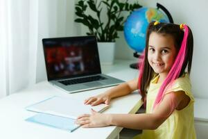 Cool online school. Kid studying online at home using a laptop. Cheerful young little girl using laptop computer studying through online e-learning system. Distance or remote learning photo