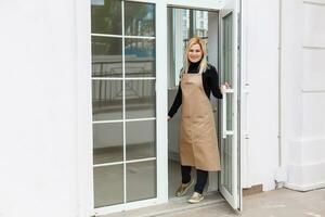Half length portrait of waitress dressed in apron with copy space for brand name open store starting work ready to serve visitors, woman entrepreneur barista standing at restaurant entrance photo