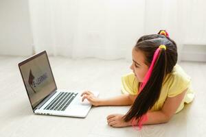 Cool online school. Kid studying online at home using a laptop. Cheerful young little girl using laptop computer studying through online e-learning system. Distance or remote learning photo