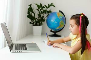 Cool online school. Kid studying online at home using a laptop. Cheerful young little girl using laptop computer studying through online e-learning system. Distance or remote learning photo
