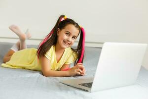 Cool online school. Kid studying online at home using a laptop. Cheerful young little girl using laptop computer studying through online e-learning system. Distance or remote learning photo