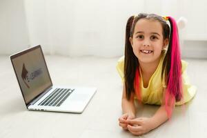 Cool online school. Kid studying online at home using a laptop. Cheerful young little girl using laptop computer studying through online e-learning system. Distance or remote learning photo