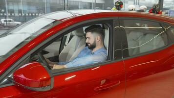 Attractive young man smiling to the camera sitting in a new car at the dealership video