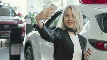 Happy woman taking selfies with keys to her new car at the dealership video