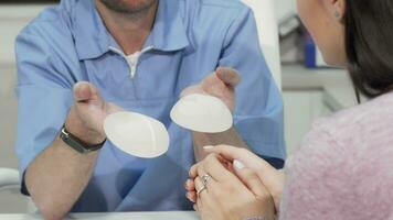 Plastic surgeon showing two breast implants to female patient video