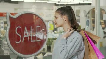 Attractive female customer holding shopping bags looking at store display video