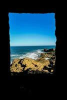 un ver de el Oceano mediante un ventana en un rocoso acantilado foto