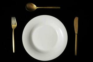 un blanco plato con oro cucharas y tenedor foto